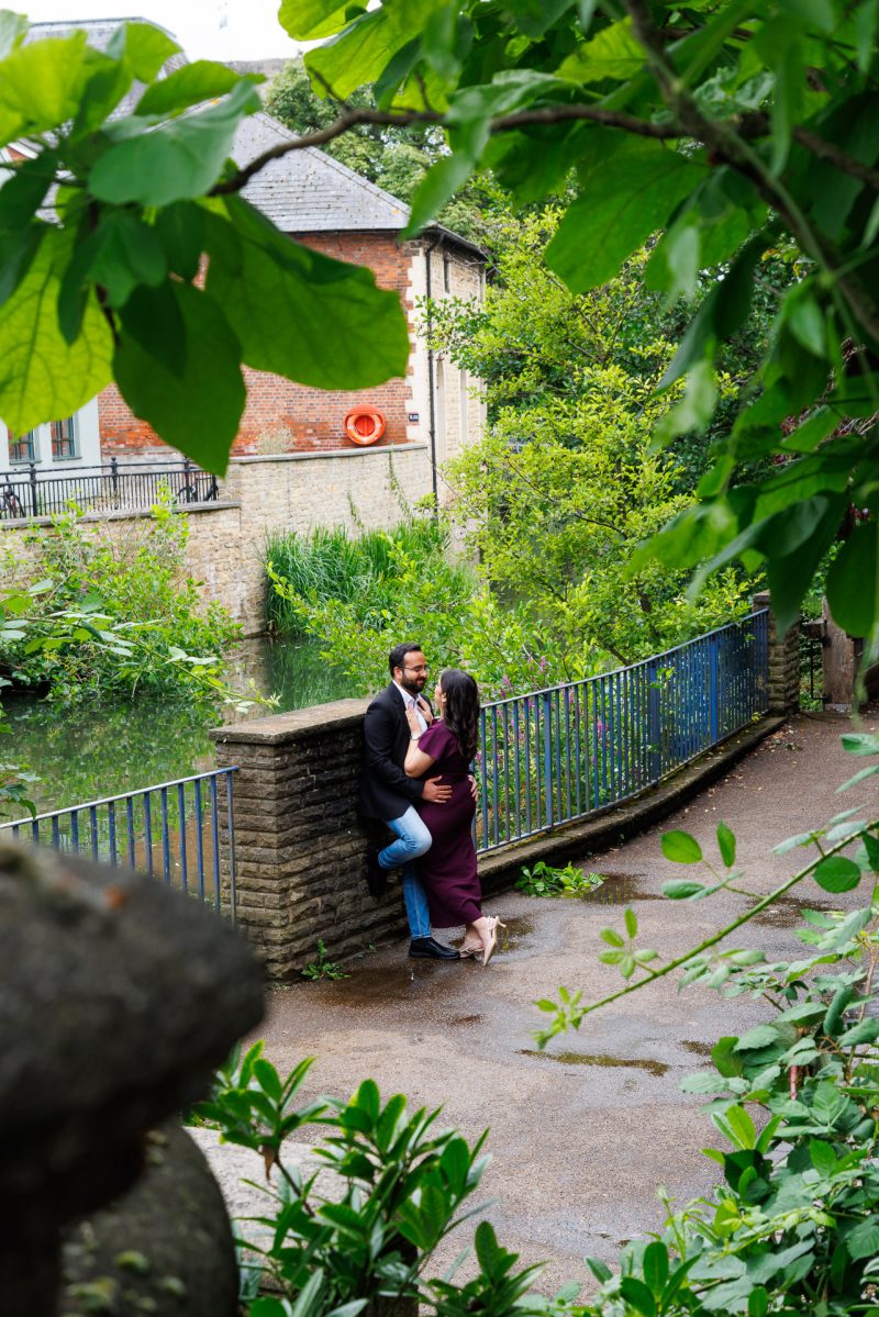 Jordan Taylor C Photography - Candid moment of couple smiling on Oxford cobblestone streets during their UK engagement shoot, standing close and looking at each other by the Canals of Oxford.