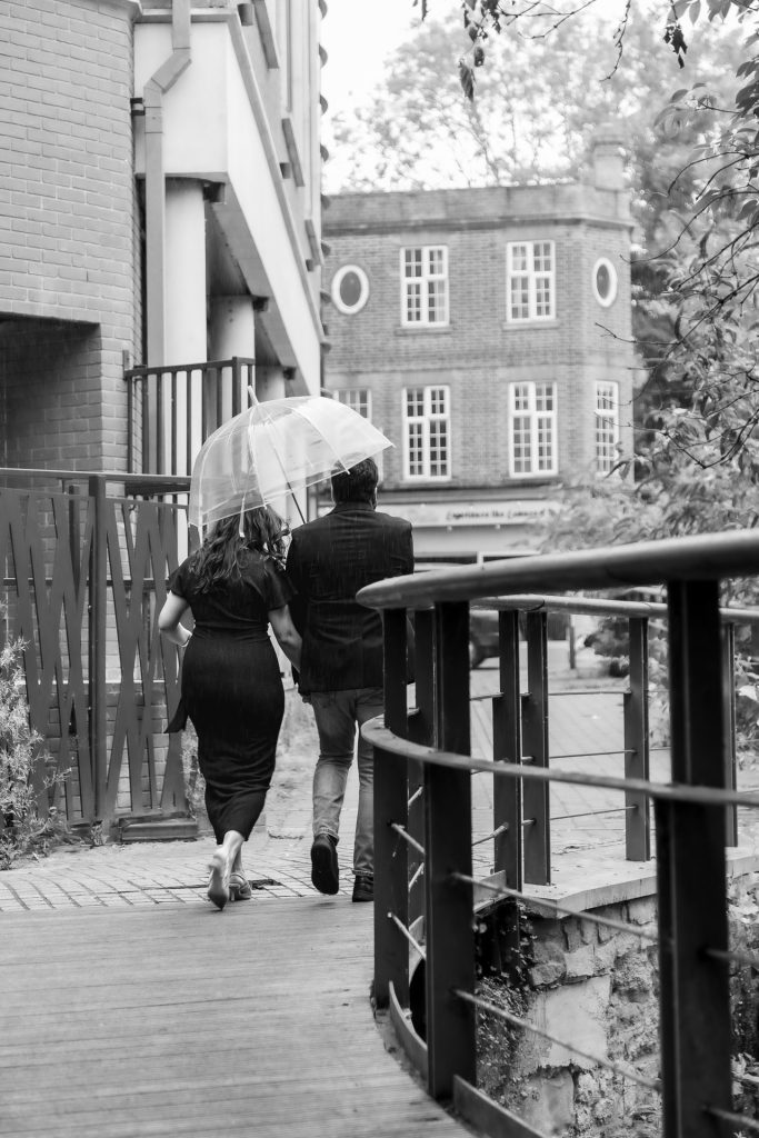 Candid moment of couple smiling on Oxford cobblestone streets during their rainy engagement shoot, during a rainy day in Oxford - Jordan Taylor C Photography