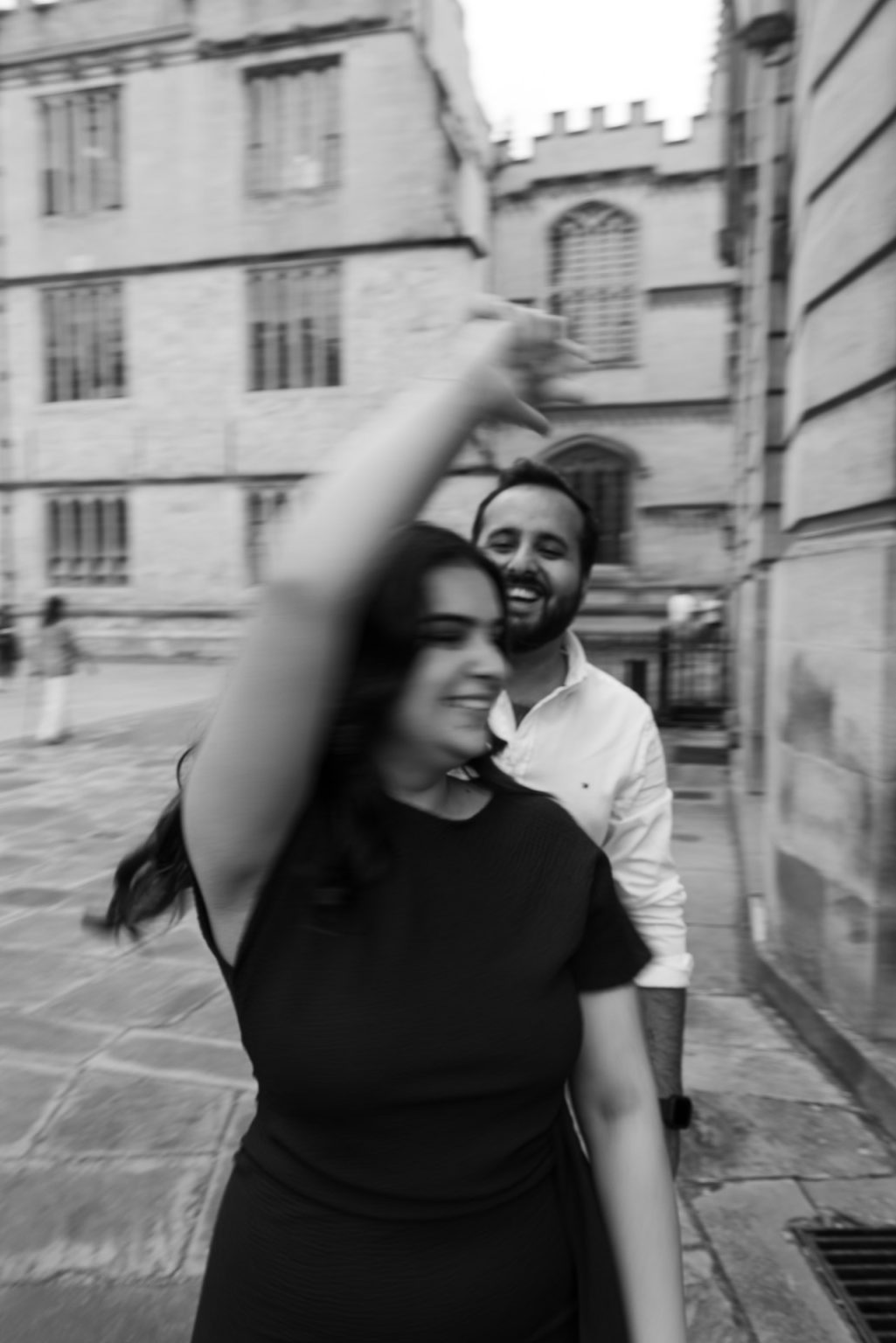 Couple laughing while he spins her in a circle, laughing during an engagement shoot in Oxford outside the Bodleian Library | Oxford engagement shoot, Oxford wedding photographer, Romantic engagement photos Oxford, UK wedding and engagement photography, Destination engagement shoot UK, London and Oxford wedding photographer, London engagement shoot, London engagement photographer