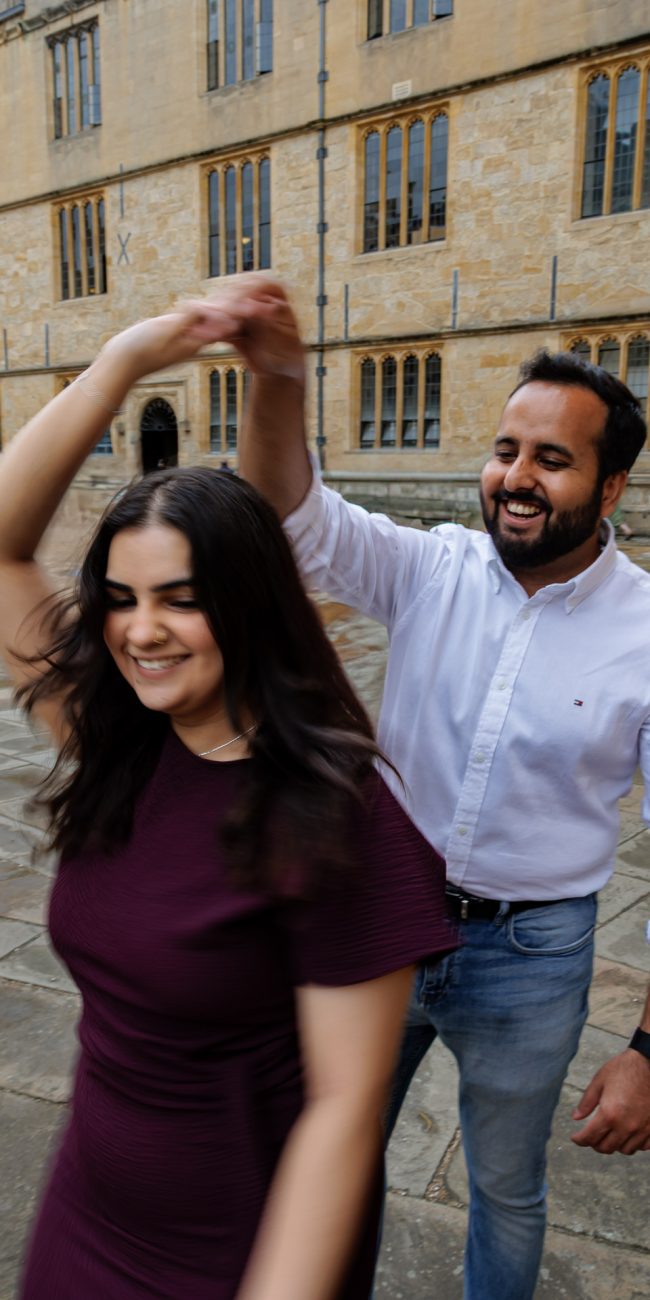 Couple laughing while he spins her in a circle, laughing during an engagement shoot in Oxford outside the Bodleian Library | Oxford engagement shoot, Oxford wedding photographer, Romantic engagement photos Oxford, UK wedding and engagement photography, Destination engagement shoot UK, London and Oxford wedding photographer, London engagement shoot, London engagement photographer