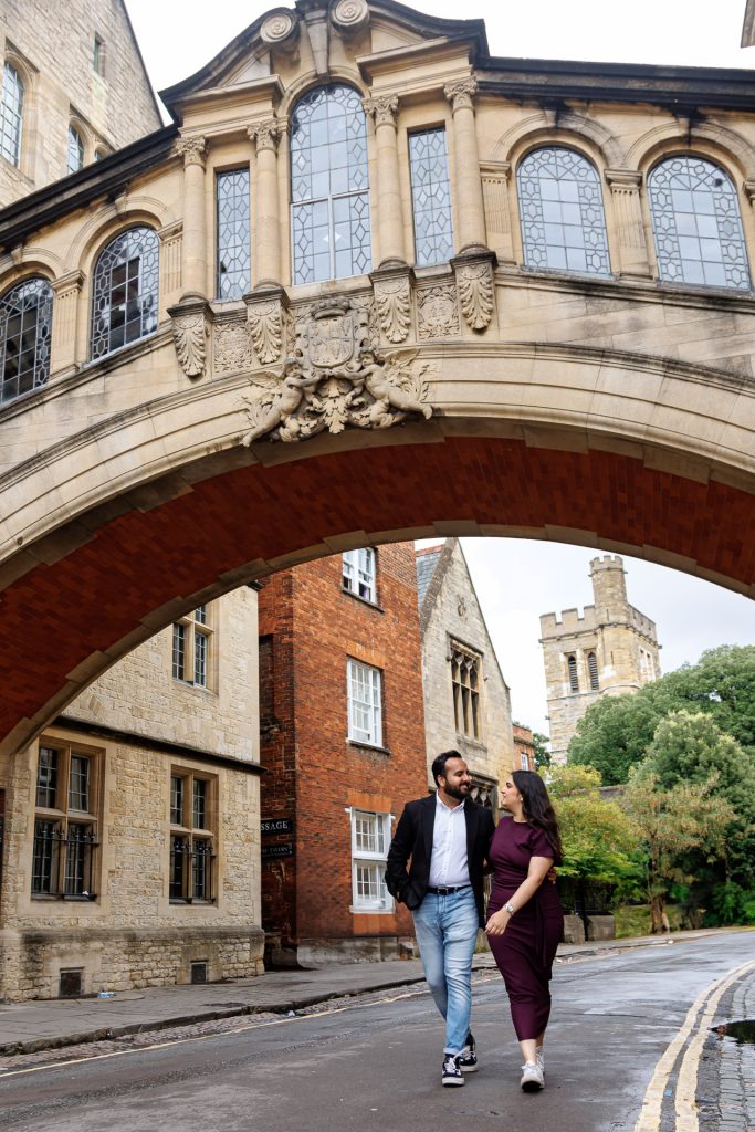 Engaged couple standing beneath the historic stone arches at Oxford University during their romantic Oxford engagement shoot, captured by a London wedding photographer. - Jordan Taylor C Photography